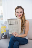 Cheerful young woman sitting on sofa holding newspaper