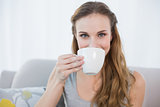 Cheerful young woman sitting on sofa holding cup