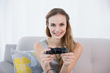 Cheerful young woman sitting on sofa playing video games