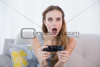 Shocked young woman sitting on sofa playing video games