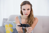 Serious young woman sitting on sofa playing video games
