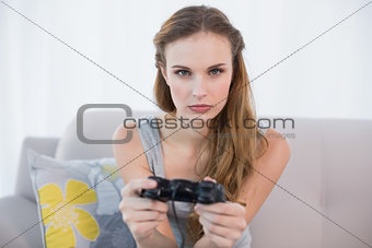 Serious young woman sitting on sofa playing video games