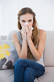 Sick woman sitting on sofa blowing her nose