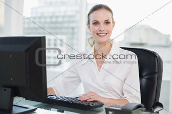 Smiling businesswoman sitting at desk looking at camera