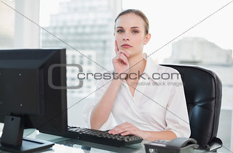 Thoughtful businesswoman sitting at desk looking at camera