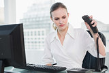 Angry businesswoman sitting at desk hanging up phone