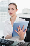 Serious businesswoman sitting at desk holding tablet pc