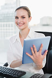Smiling businesswoman sitting at desk holding tablet pc
