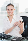 Smiling businesswoman sitting at desk sending a text