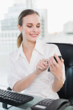 Happy businesswoman sitting at desk sending a text