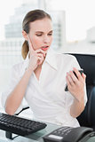 Thoughtful businesswoman sitting at desk sending a text