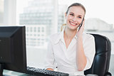 Smiling businesswoman sitting at desk talking on smartphone