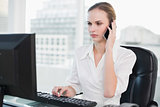 Serious businesswoman sitting at desk talking on smartphone looking at screen