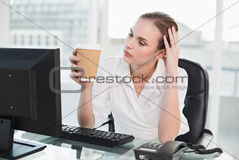 Tired businesswoman holding disposable cup sitting at desk