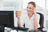Smiling businesswoman holding disposable cup sitting at desk
