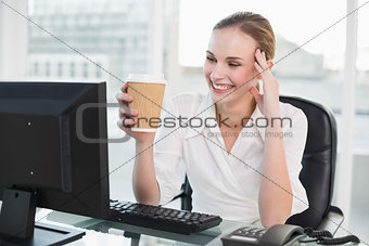 Smiling businesswoman holding disposable cup sitting at desk