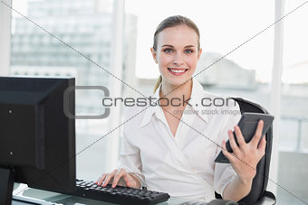 Happy businesswoman holding calculator sitting at desk