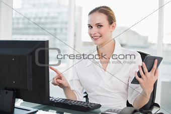 Cheerful businesswoman holding calculator sitting at desk looking at camera