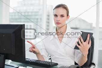 Frowning businesswoman holding calculator sitting at desk looking at camera