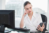 Frowning businesswoman holding calculator sitting at desk