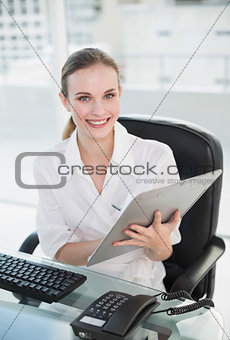 Happy businesswoman writing on clipboard sitting at desk
