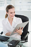 Smiling businesswoman writing on clipboard sitting at desk