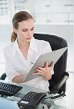 Serious businesswoman writing on clipboard sitting at desk
