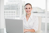 Happy businesswoman using laptop looking at camera