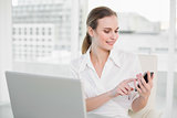 Happy businesswoman using laptop and texting on smartphone