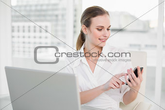 Happy businesswoman using laptop and texting on smartphone