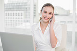 Cheerful businesswoman using laptop and making a call