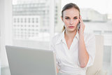 Frowning businesswoman using laptop and making a call