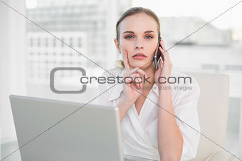 Thoughtful businesswoman using laptop and making a call looking at camera