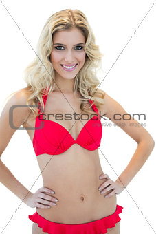 Openly smiling blonde model posing with hands on hips in red bikini