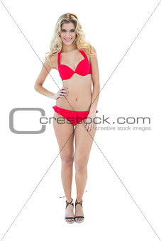 Gleeful blonde model posing with hand on hips wearing red bikini
