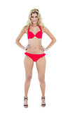 Cheerful smiling blonde model posing with hands on hips wearing red bikini