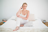 Natural smiling blonde phoning while sitting on bed