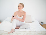 Natural content blonde holding smartphone while sitting on bed