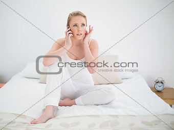 Natural concentrating blonde holding smartphone while sitting on bed