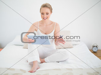 Natural smiling blonde looking at tablet while sitting on bed