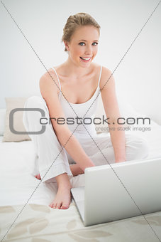 Natural happy blonde sitting in front of laptop on bed