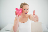 Natural happy blonde holding piggy bank while sitting on bed