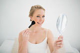 Natural happy blonde holding mirror and using brush