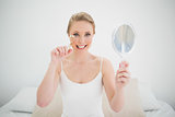 Natural happy blonde holding mirror and using eyelash curler