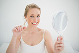 Natural smiling blonde holding mirror and eyelash curler