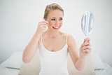 Natural cheerful blonde holding mirror and using tweezers