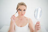 Natural stern blonde holding mirror and using eyebrow brush