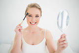 Natural smiling blonde holding mirror and using eyebrow brush