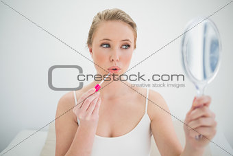 Natural calm blonde holding mirror and applying lip gloss