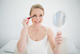 Natural cheerful blonde holding mirror and applying mascara